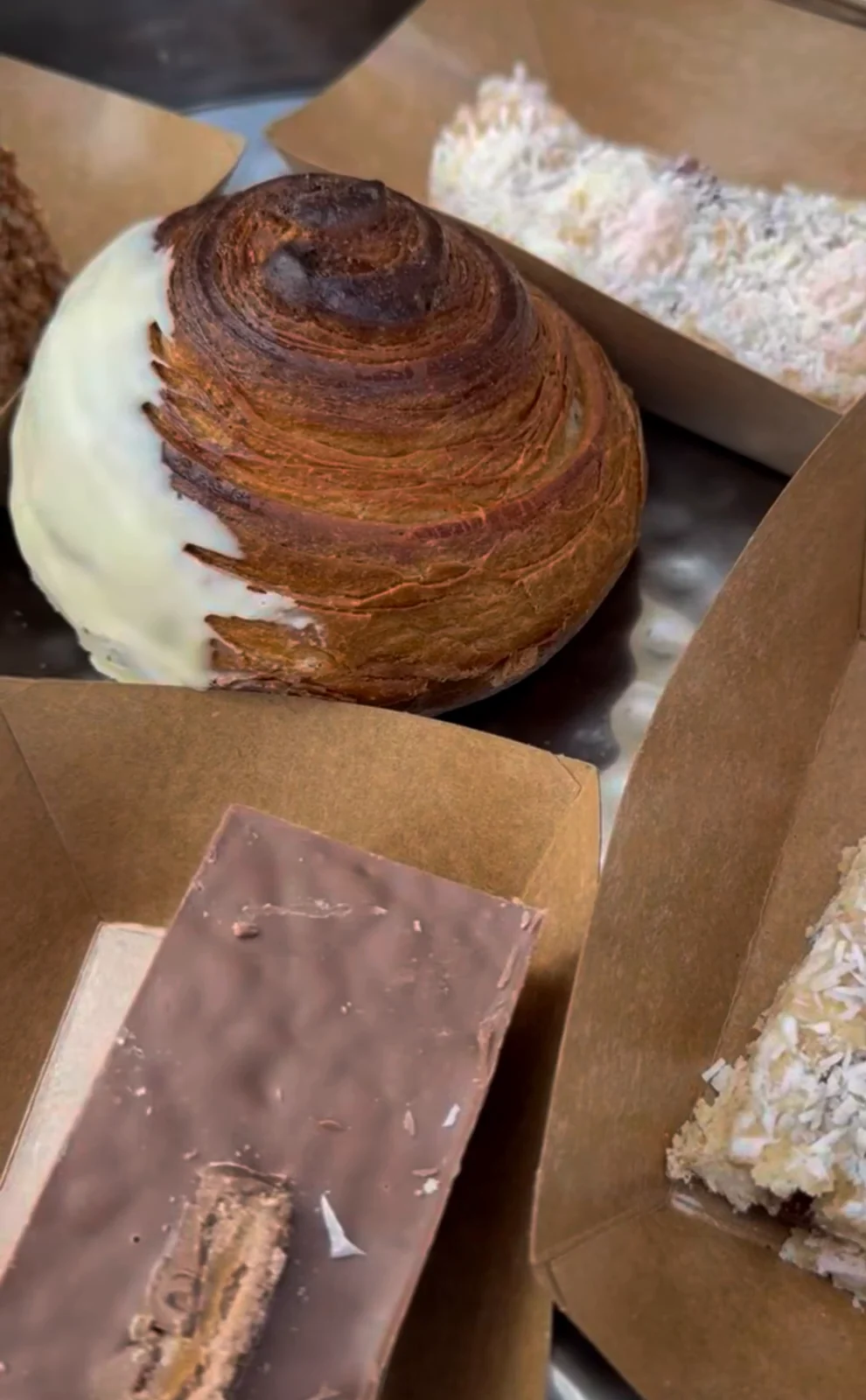 Homebaked goods in kraft trays: a white-chocolate-dipped pastry swirl, a chocolate bar and a coconut traybake